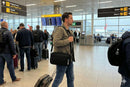 Man at airport carrying black crossbody bag and rolling suitcase near departure gates